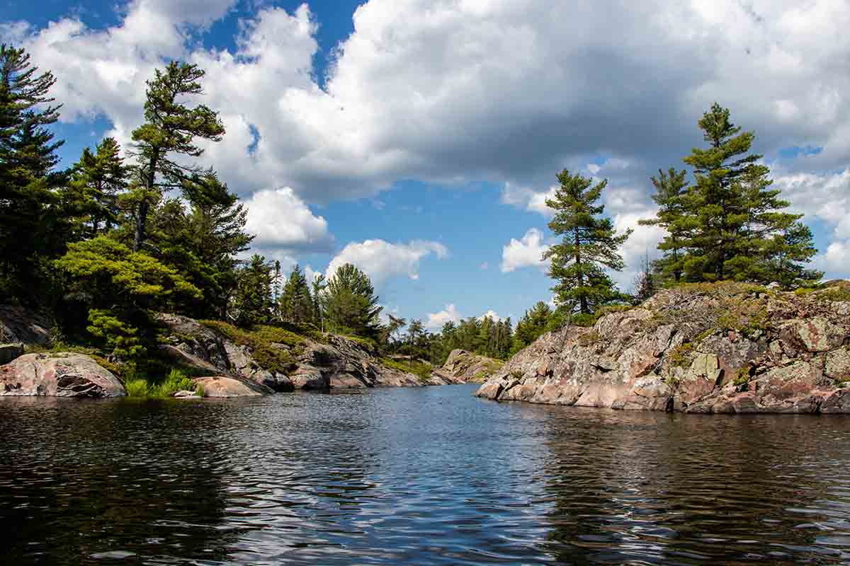 Rocks, trees, blue sky, white clouds and water on a summer day on river