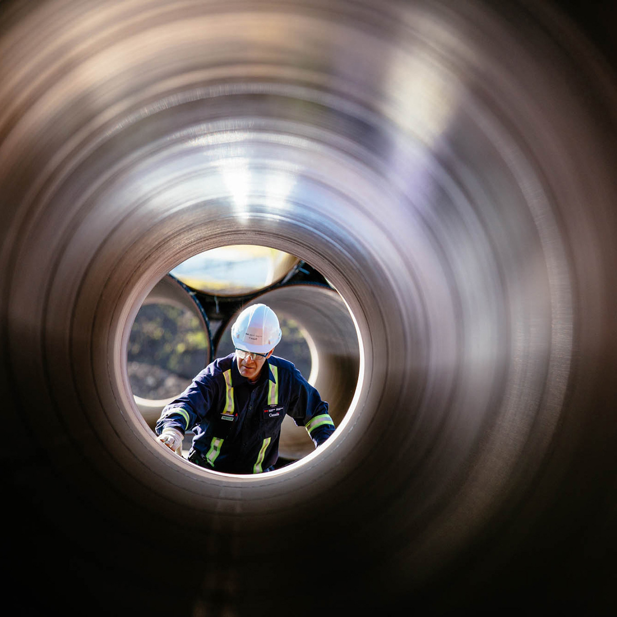 Person wearing personal protective equipment inspecting the inside of a large pipe.