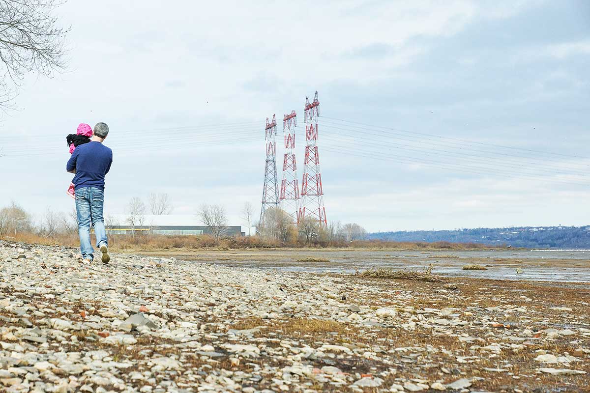 Figure 1 – On the bank of a waterway, a man walks with a child in the direction of three electricity pylons.