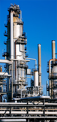 Detailed view of distillation towers at a refinery, against a bright blue sky.