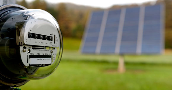 Gas meter in the foreground with a solar panel out of focus in the background