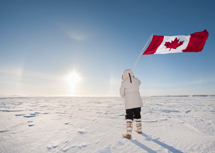 A woman dressed in a white parka holds up a Canadian flag against the snowy horizon