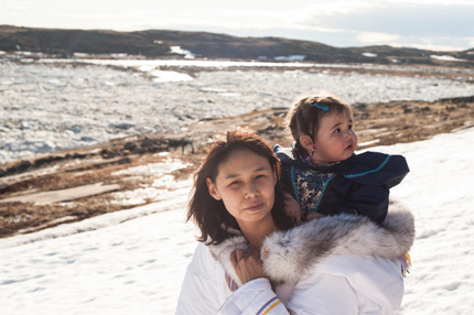 An Inuit woman carries her infant on her back as they traverse the snowy tundra