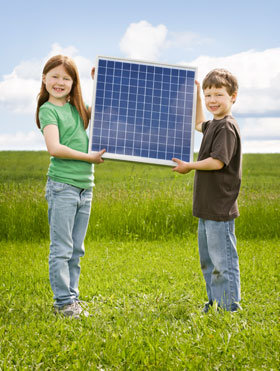 Two children, a boy and girl, hold up a solar panel in a field of grass