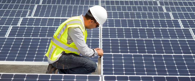 Technicien avec casque et veste de sécurité examinant des panneaux solaires sur le toit d’un édifice