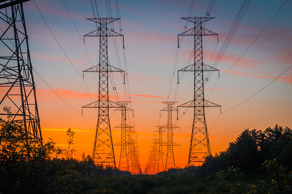 Lignes de transport d’électricité s’évanouissant à l’horizon sous un coucher de soleil orange.