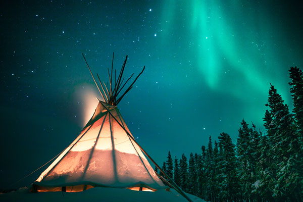 Glowing teepee in the snowy forest under the northern lights, Yellowknife.
