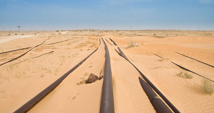 Pipelines dans le désert partiellement recouverts de sable avec lignes de transport d’électricité à l’horizon