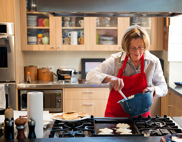 Dame portant un tablier rouge qui fait cuire des crêpes sur une cuisinière au gaz.
