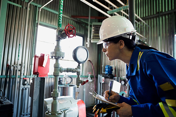 An engineer in personal protective gear inspects a pressure valve in a natural gas plant.