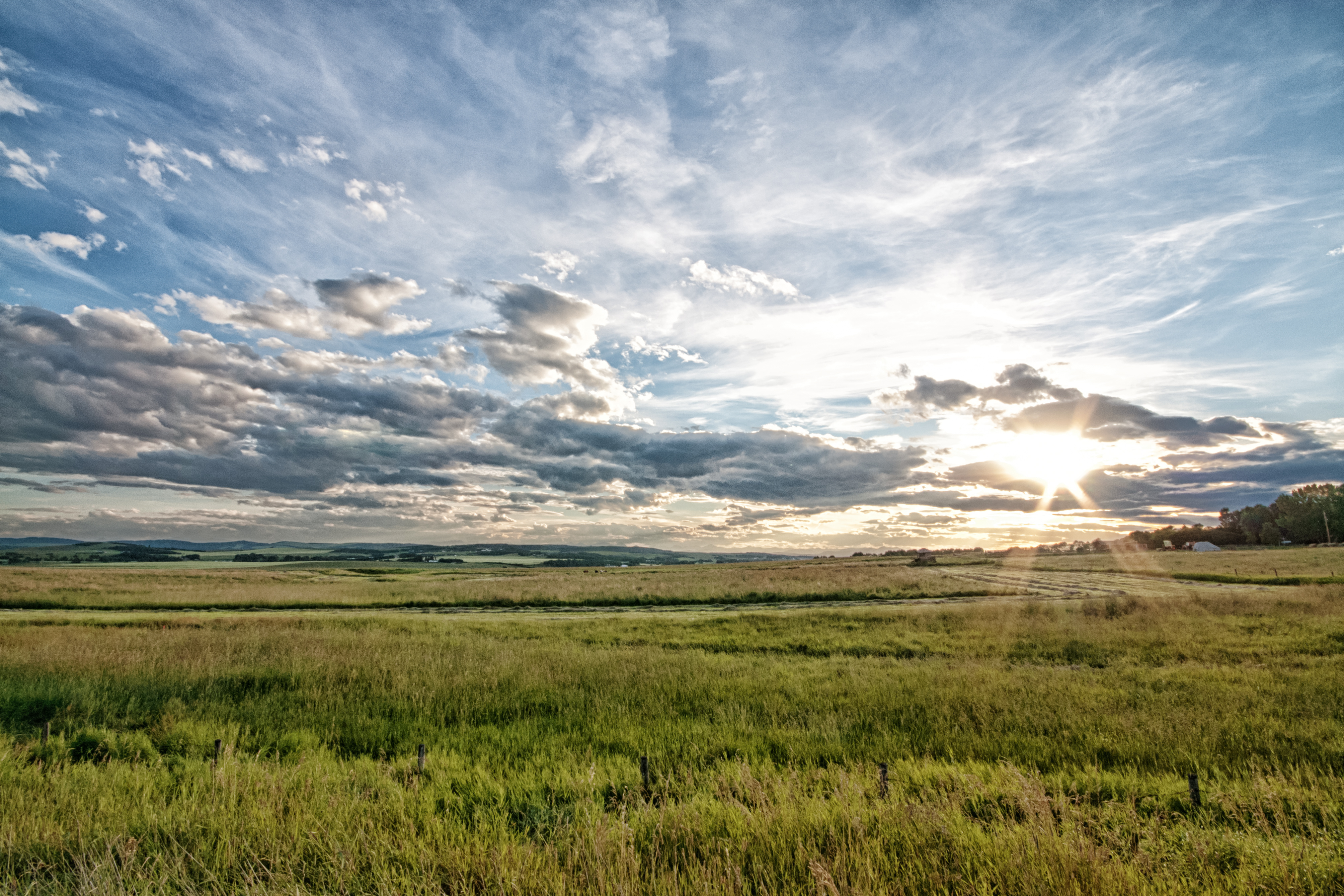 Sun setting on Alberta prairie grassland with some clouds in the sky.
