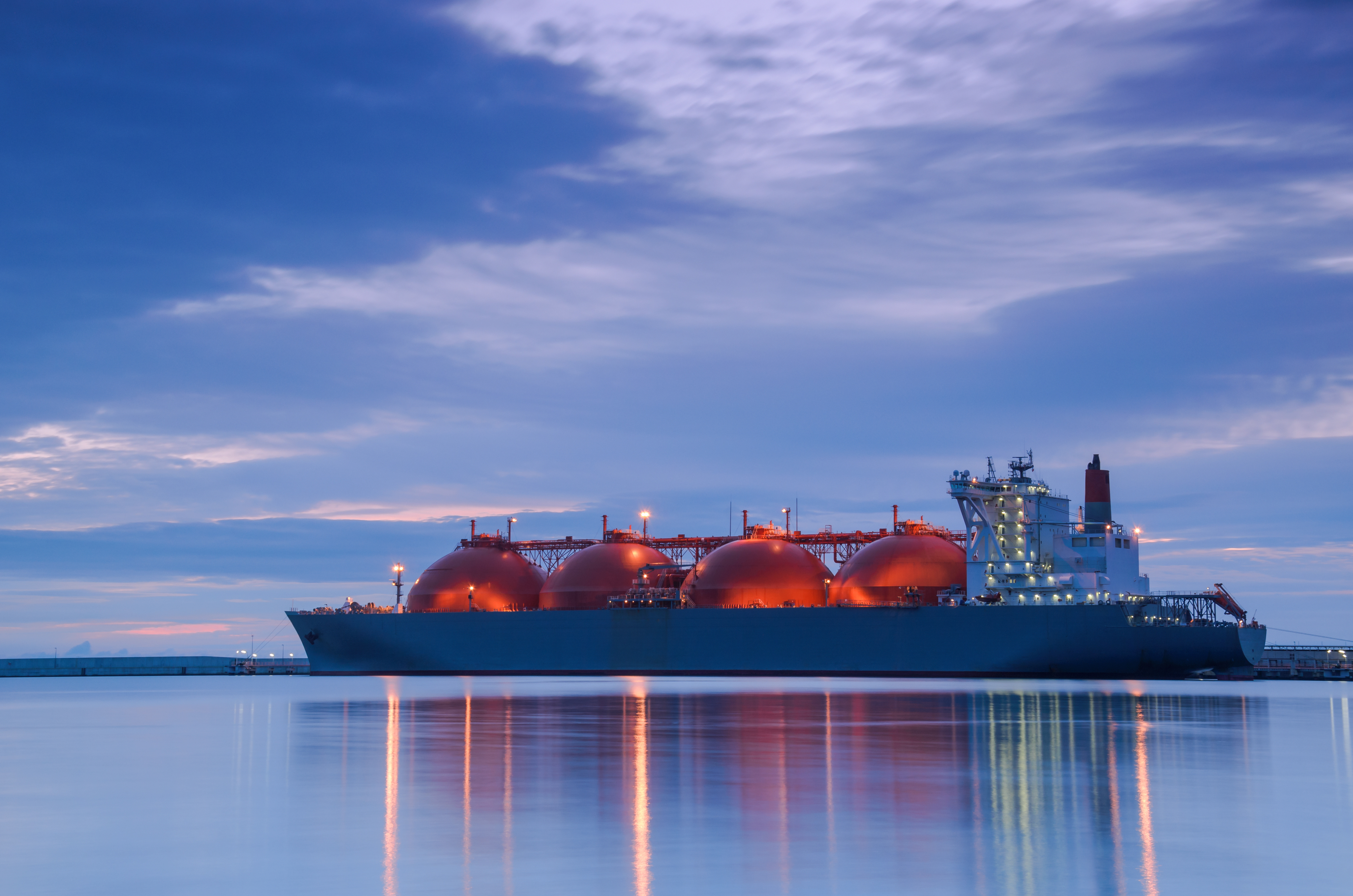 Liquid natural gas (LNG) tanker sails on smooth waters at dusk.