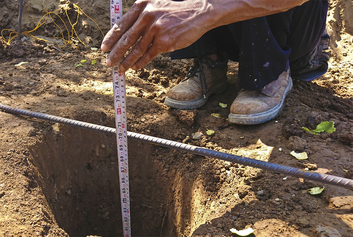 Travailleur mesurant la profondeur d’un trou dans la terre