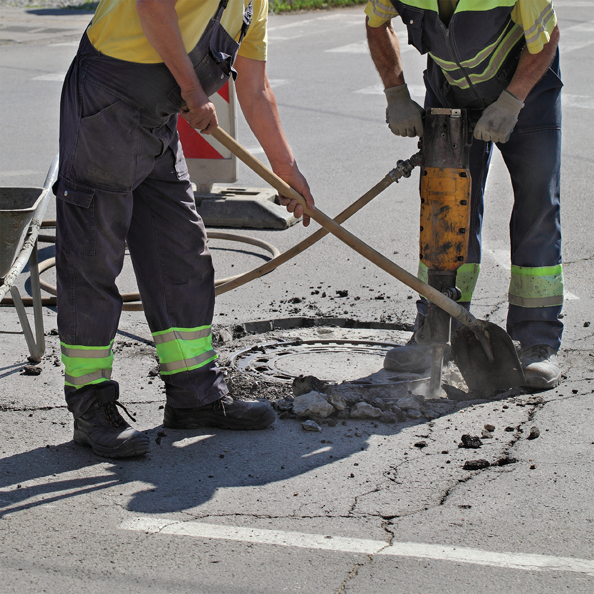 Workers near sewer manhole chipping asphalt with jackhammer