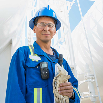Male employee wearing PPE, holding gloves with whiteinfrastructure in the background.