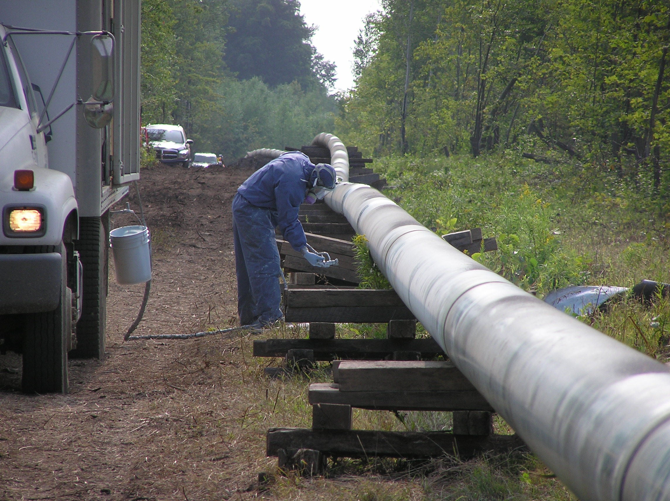Un travailleur portant un masque à gaz inspecte un pipeline près d’un camion.