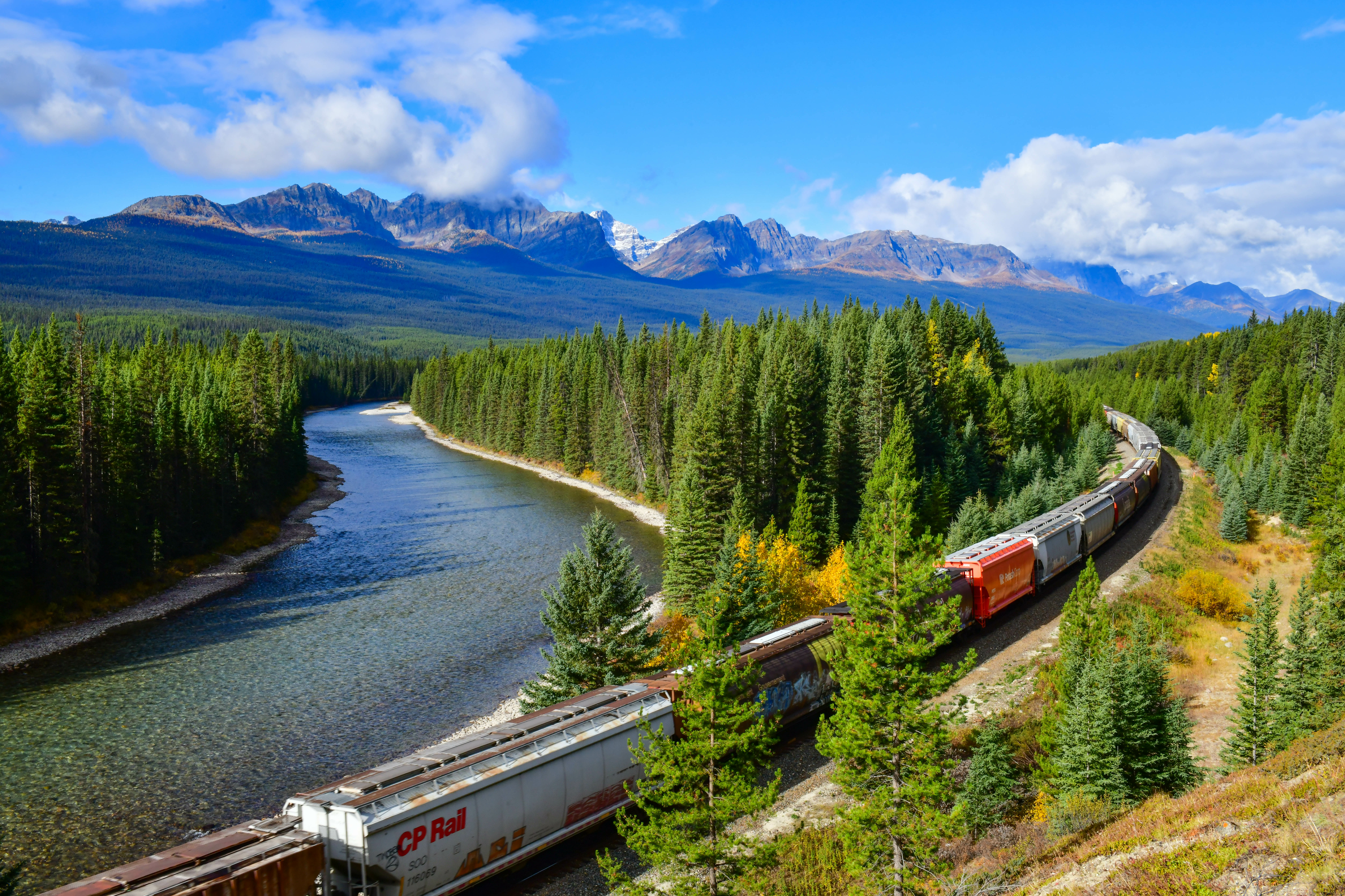 Sur un arrière-plan de montagnes, un train de CP longe une rivière en traversant les Rocheuses de l’Alberta.